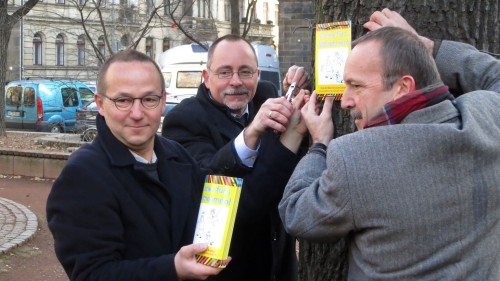 Pfarrer, Ortsamtsleiter und Grünflächen-Chef hängen eine Tafel auf.