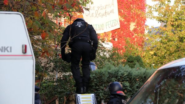 Mehrere Polizisten klettern über den Zaun auf das Grundstück.