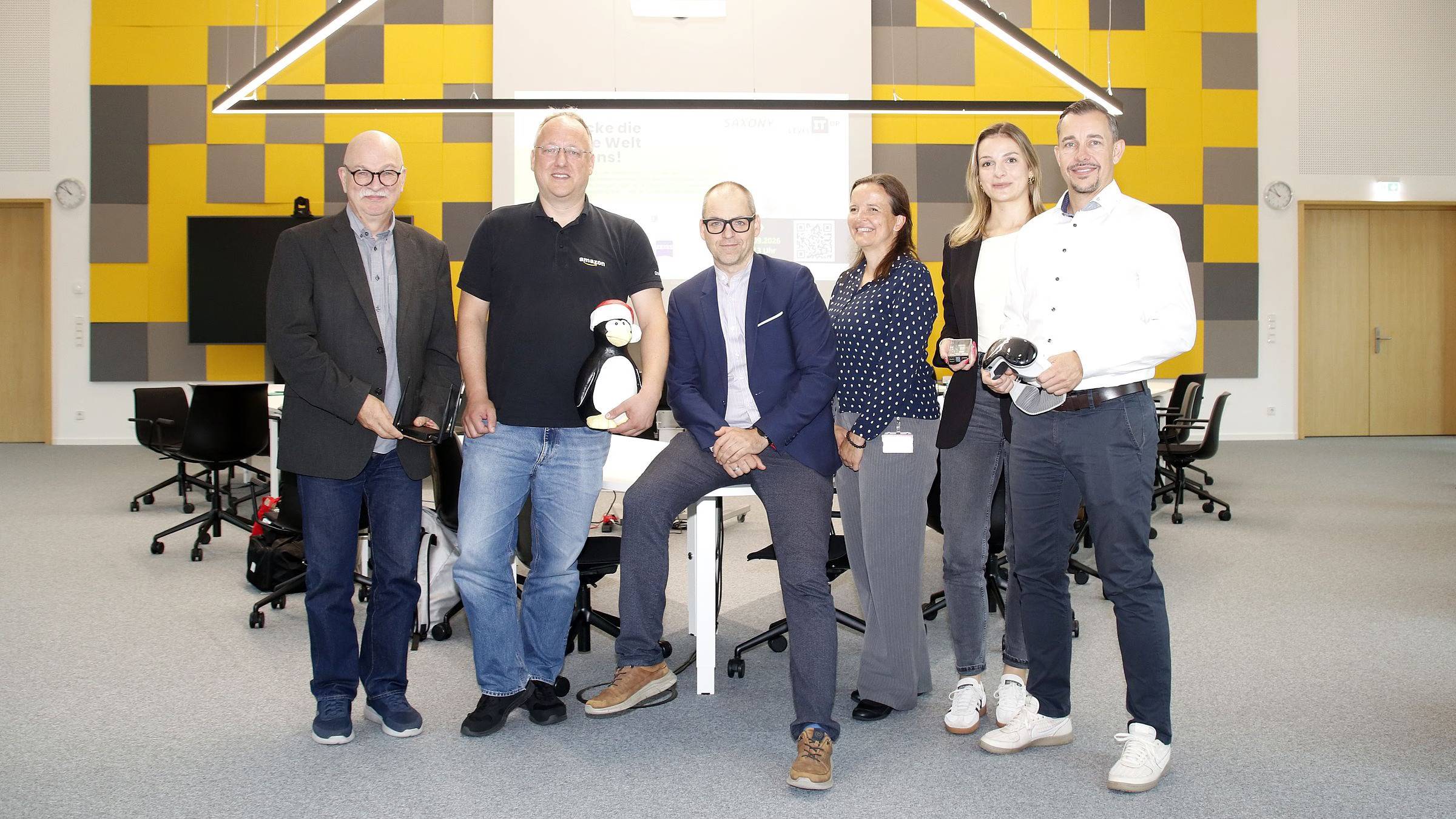 Schnuppertag zum „Level IT Up“-Tag 2026. Es laden ein (von links nach rechts): Friedemann Höller (Eigenbetrieb IT Landeshauptstadt Dresden), Andreas Stieger (AWS Development Center Germany – hier mit Linux-Pinguin), Frank Bösenberg (Silicon Saxony – hier mit Augmented-Reality-Brille), Jenny Wätzig (SachsenEnergie), Anne-Sophie Graf (Communardo) und René Wohllebe (SAP). Foto: Anton Launer